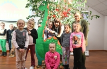 Dzieci stojące przy makiecie dinozaura. Za nimi roślinka 