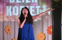 Kobieta śpiewająca do mikrofonu. Drugą ręką szeroko wymachuje 