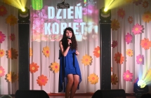 Kobieta śpiewająca do mikrofonu - w tle baner z napisem - Dzień Kobiet 