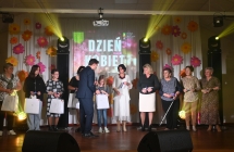 Mężczyzna w garniturze wręczający kobietom na scenie upominki 