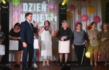 Mężczyzna w towarzystwie kilku kobiet na scenie. Kobiety trzymają drobne upominki 