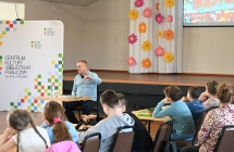 Mężczyzna mówiący do grupy kilkudziesięciorga dzieci 