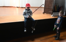 Dwoje chłopców. Jeden siedzący z wędką na scenie, drugi stoi obok niego pod sceną. 