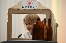 Dziewczynka siedząca na scenie. Widać ją przez okienko z napisem - apteka 