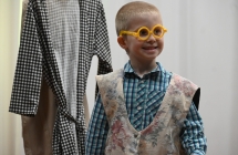 Uśmiechnięty chłopiec w okularach i serdaku na scenie podc zas odgrywania roli aktorskiej 