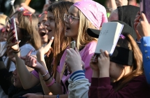 Kilkanaście osób śpiewających za barierkami piosenkę swojego idola podczas koncertu 