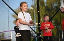 Uśmiechnięta dziewczynka i jej rówieśnicy na scenie podczas pokazu tanecznego 