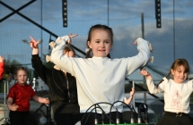 Uśmiechnięta dziewczynka na scenie. Za nią rówieśnicy 