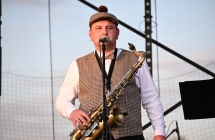 Mężczyzna w ludowym stroju śpiewa do mikrofonu - trzyma również saksofon 