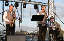 Troje mężczyzn w ludowych strojach - dwoje z nich grają na saksofonach, jeden na akordeonie 