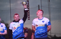 Dwoje mężczyzn na scenie. Jeden w górze trzyma puchar 