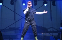 Mężczyzna śpiewający na scenie. W jednej ręce trzyma mikrofon, drugą ma wyłożoną w bok 