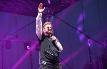 Mężczyzna z podniesioną w górze ręką. W drugiej trzyma mikrofon 