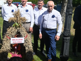 Czworo elegancko ubranych mężczyzn prezentujących wieniec dożynkowy 