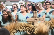Kilka jednakowo ubranych kobiet stojących przy wieńcu dozynkowym 