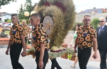 Troje mężczyzn w jednakowych koszulach niosący wieniec dożynkowy 