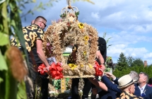 Kilkoro mężczyzn kładących na wóz wieniec dożynkowy 