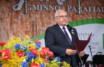Mężczyzna w garniturze przemawiający na scenie do mikrofonu 