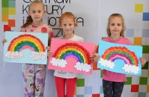 Trzy uśmiechnięte dziewczynki z pracami plastycznymi