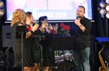 Trzy kobiety i mężczyzna na scenie. Mężczyzna śpiewa do mikrofonu