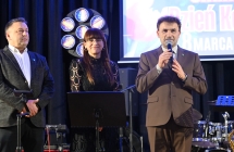 Dwóch mężczyzn i kobieta na scenie. Mężczyzna mówi do mikrofonu